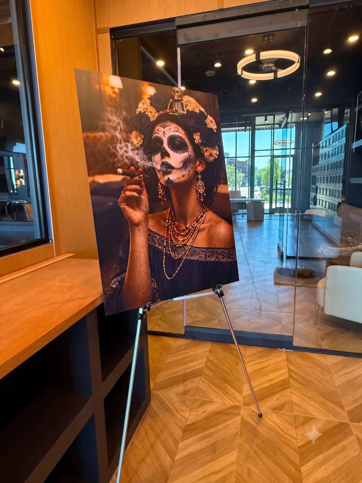 La Catrina art print on an easel inside the Caballeros lounge — a Day of the Dead woman with sugar skull makeup holding a lit cigar